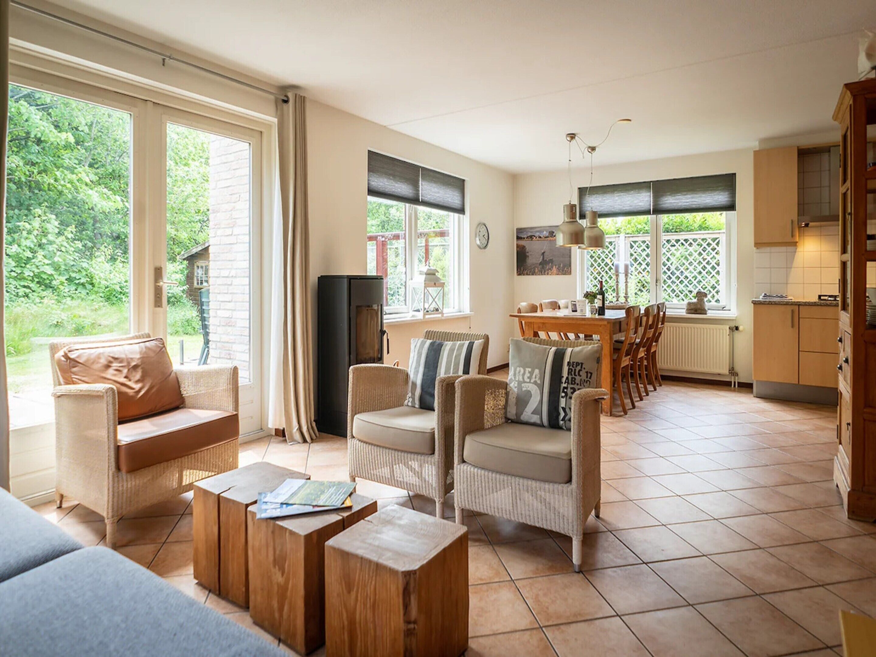 A spacious living area with a sofa, chairs, a coffee table, a dining table, and a kitchen in the background.