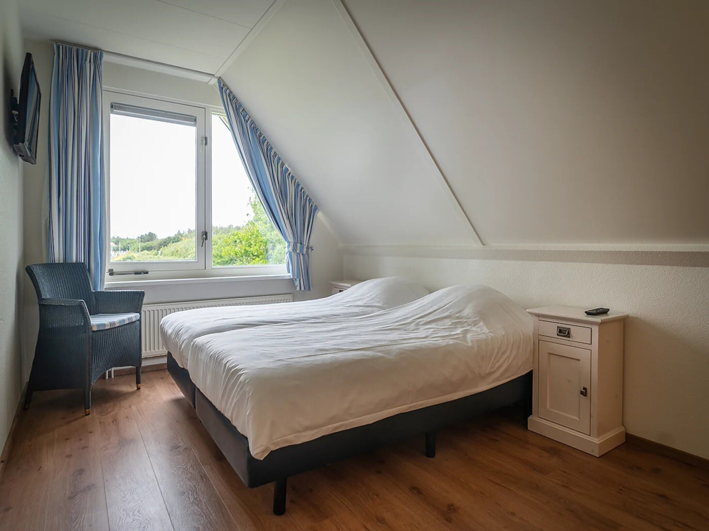 Une chambre à coucher avec un lit, une chaise, une table de chevet et une fenêtre avec des rideaux.