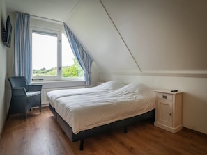 Ein Schlafzimmer mit Bett, Sessel, Nachttisch und einem Fenster mit Vorhängen.