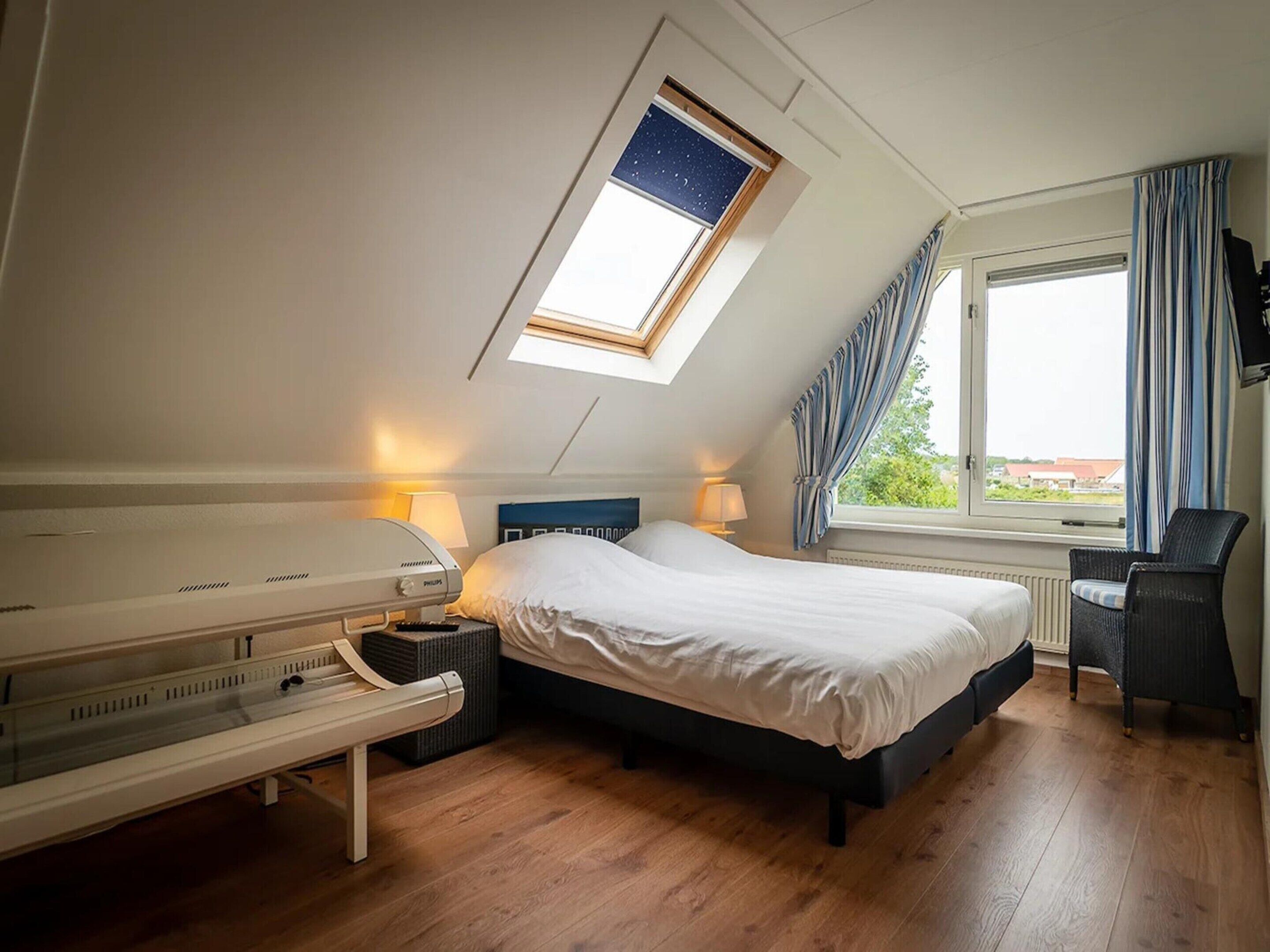 Een hotelkamer met een bed, bedlampen, een verwarming, een raam met gordijnen en een dakraam.