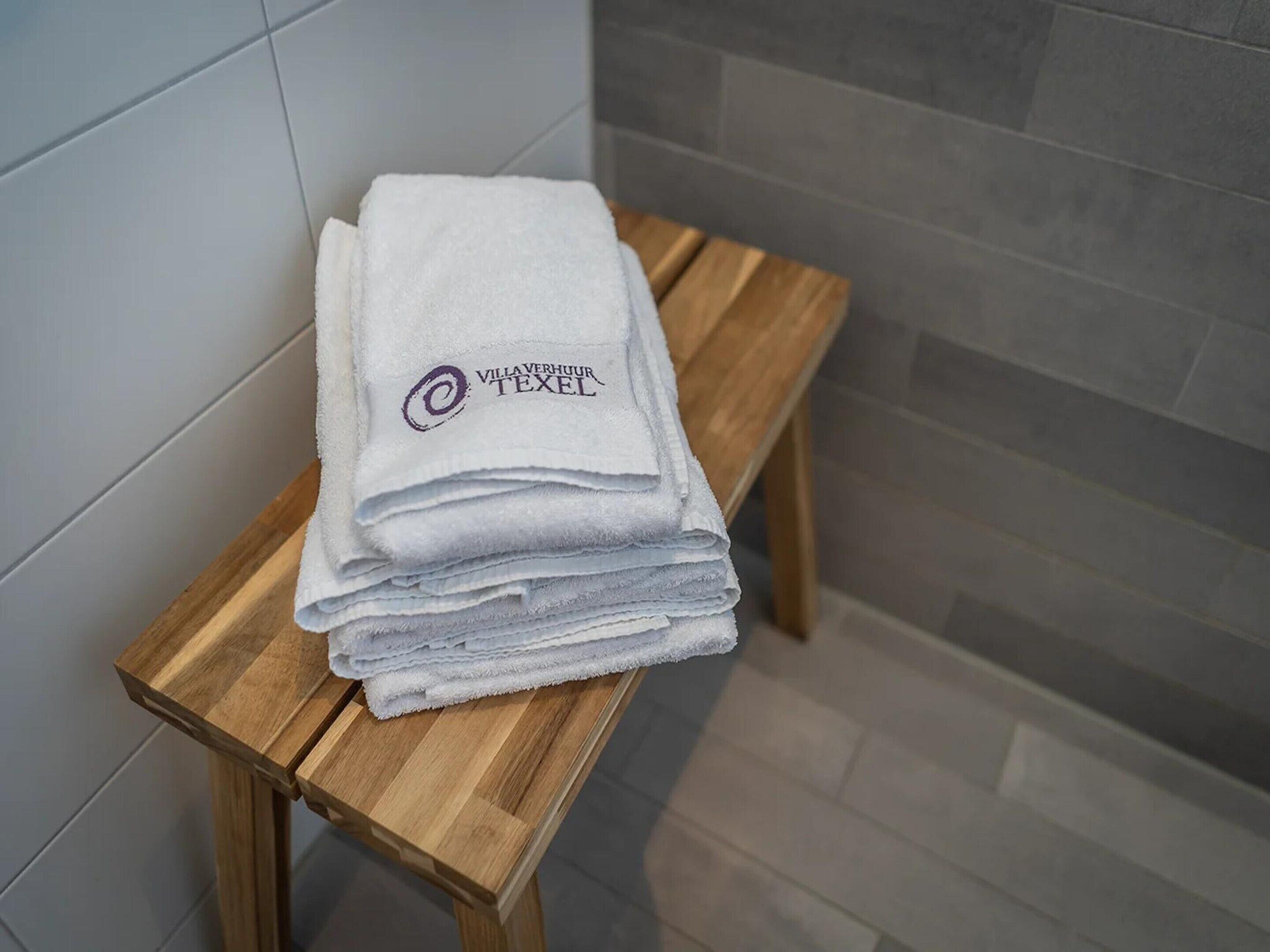 Un montón de toallas blancas con un logotipo sobre un taburete de madera en un baño.