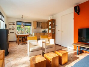 A modern living room with a dining area, kitchen, and a TV mounted on an orange wall. - Spa Retreat With Private Sauna (De Koog)