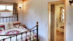 A bedroom with a bed, a wooden ceiling, a window with curtains, and a door leading to another room.