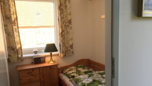 A small bedroom with a single bed, a wooden dresser, a radio, and a window with curtains.