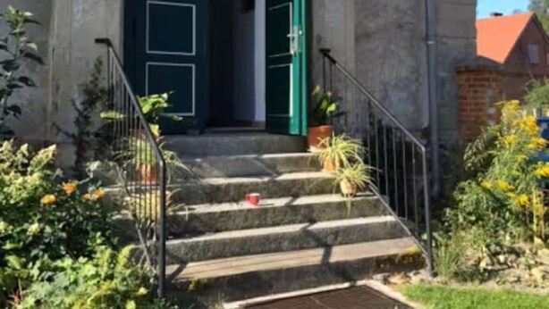 A building with a concrete facade, a green door, and a set of stone steps leading to a small porch area.
