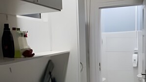 A modern bathroom with a white sink, mirror, and toilet. There is a shower area with a glass door and a towel rack.