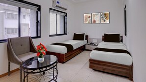 A hotel room with two beds, a chair, a table with a vase of flowers, and artwork on the wall. - Collection O Rajkot Central Bus Terminal (Rajkot)