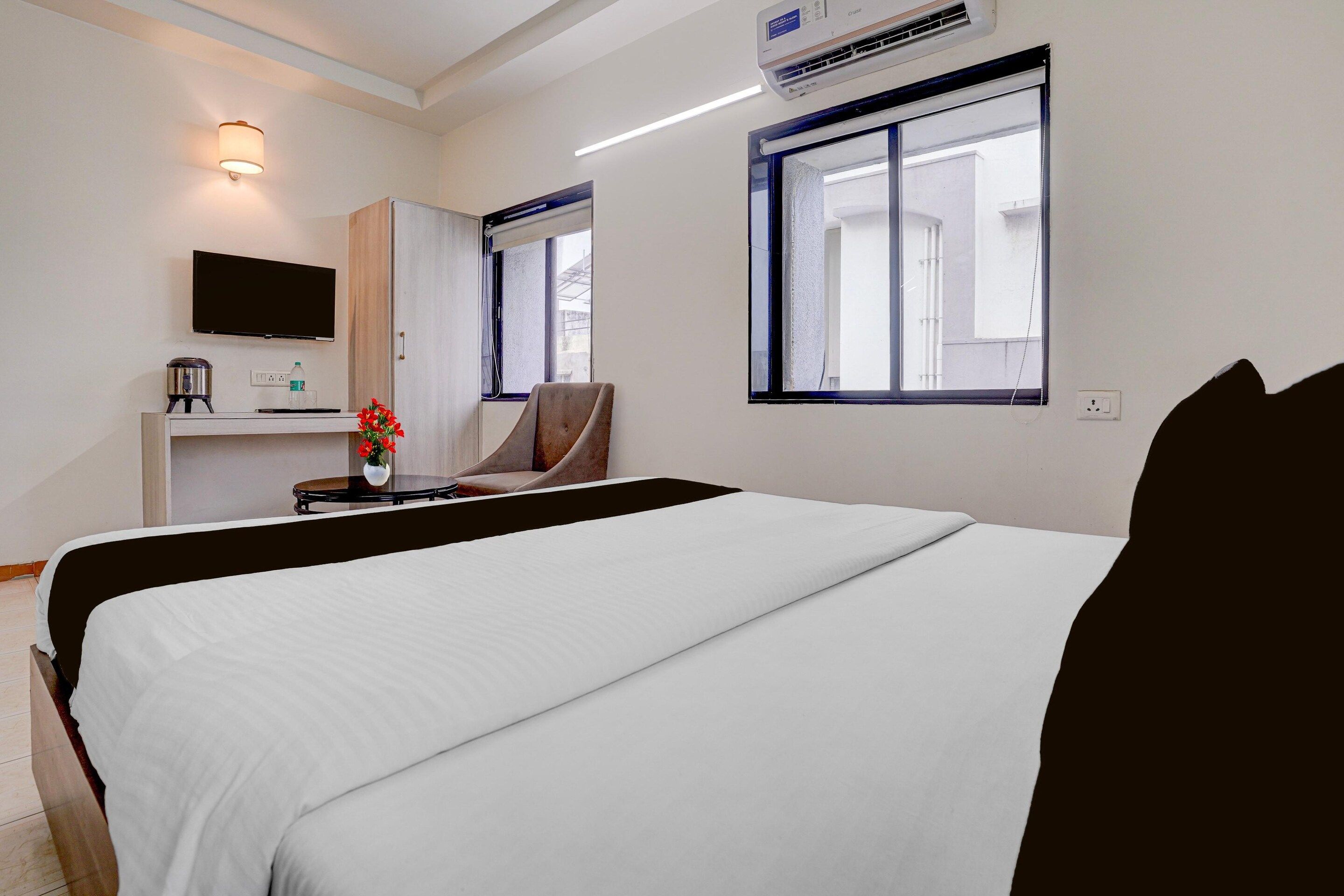 A hotel room with a bed, a desk with a television, a chair, and a window.