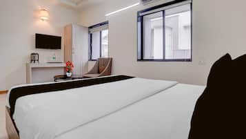 A hotel room with a bed, a desk with a television, a chair, and a window.