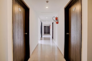 A hotel corridor with wooden doors, a fire extinguisher mounted on the wall, and a tiled floor.