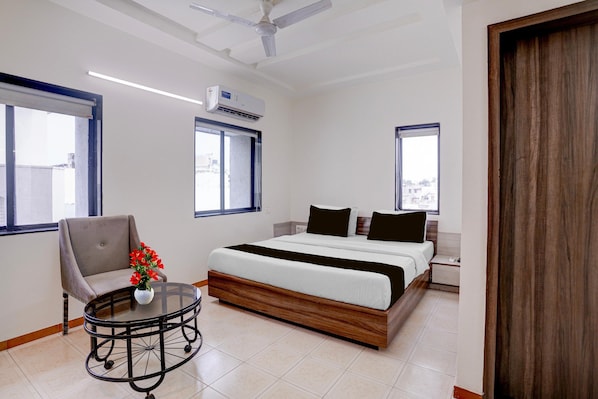 A hotel room with a bed, a chair, a small table, and a window.