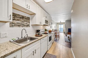 A modern kitchen with white cabinetry, a granite countertop, and a backsplash with multicolored tiles. - Oceanfront Bliss, Top Floor, 2BR, Indoor Pool & Hot Tub, Free Parking, Elevators (North Myrtle Beach)
