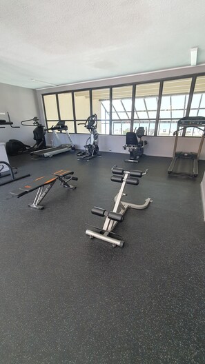 A gym with various exercise equipment, large windows, and a black rubber floor.