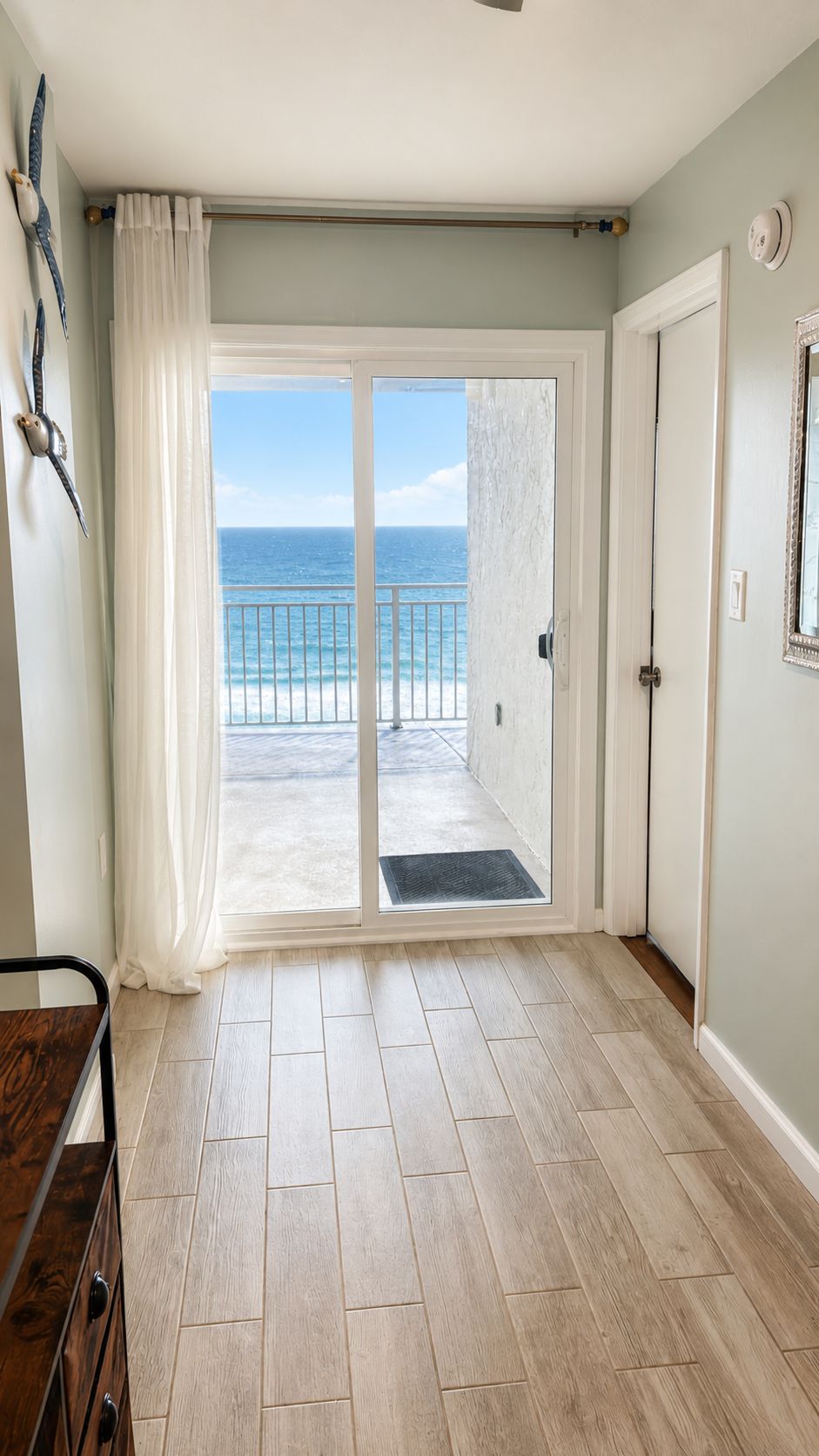 Ein Zimmer mit Holzboden, einer Tür, die auf einen Balkon mit Meerblick führt, und einer kleinen Matte im Eingangsbereich.