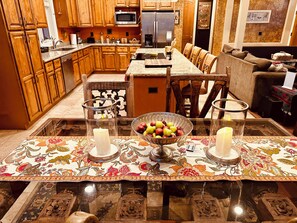 A kitchen with wooden cabinets, a microwave, a refrigerator, and a dining area with a table set for two. - Stunning Superstition Views-Hiking, Golf, Adventure. (Apache Junction)