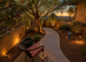 A curved pathway leading to a seating area with a chair and a small table, surrounded by desert plants and a sunset view. - Stunning Superstition Views-Hiking, Golf, Adventure. (Apache Junction)
