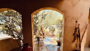 Un arco de entrada que da a un espacio exterior con un patio, una maceta roja y un jarrón con ramas.
