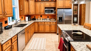 Una cocina con armarios de madera, encimeras de granito, refrigerador de acero inoxidable, microondas y estufa.