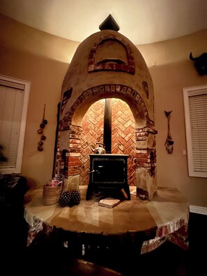 A room with a brick fireplace, a wooden table, and a window with blinds. - Stunning Superstition Views-Hiking, Golf, Adventure. (Apache Junction)