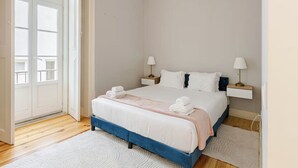 Un dormitorio con una cama, dos mesitas de noche, una puerta y un ventanal.