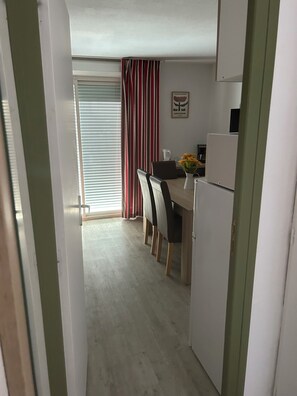 Eine kleine Küche mit Essbereich, einem Kühlschrank und einem Fenster mit Jalousien.
