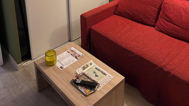 Ein Zimmer mit einem roten Sofa, einem Holztisch mit Zeitschriften, einer Lampe und einem gerahmten Zitat an der Wand.