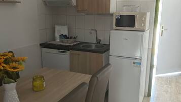 Une cuisine de taille réduite, dotée de meubles en bois, d’un four à micro-ondes, d’un évier et d’un réfrigérateur.