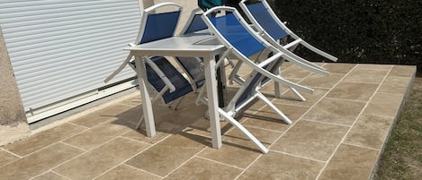 Ein Patio mit Tisch und vier Stühlen, einer weißen Rolltür und einem grünen Sonnenschirm.