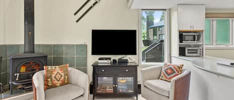 A modern living room with a fireplace, a flat-screen TV, and a kitchen area with a microwave.