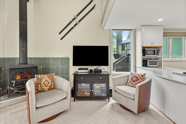 A modern living room with a fireplace, a flat-screen TV, and a kitchen area with a microwave.