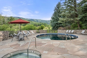 A pool area with a hot tub, lounge chairs, and a red umbrella.