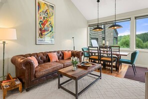 A living room with a leather sofa, a coffee table, and a dining area with chairs and a table.
