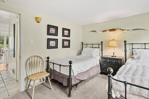 A bedroom with two beds, a chair, a bedside table, a lamp, and framed pictures on the wall.