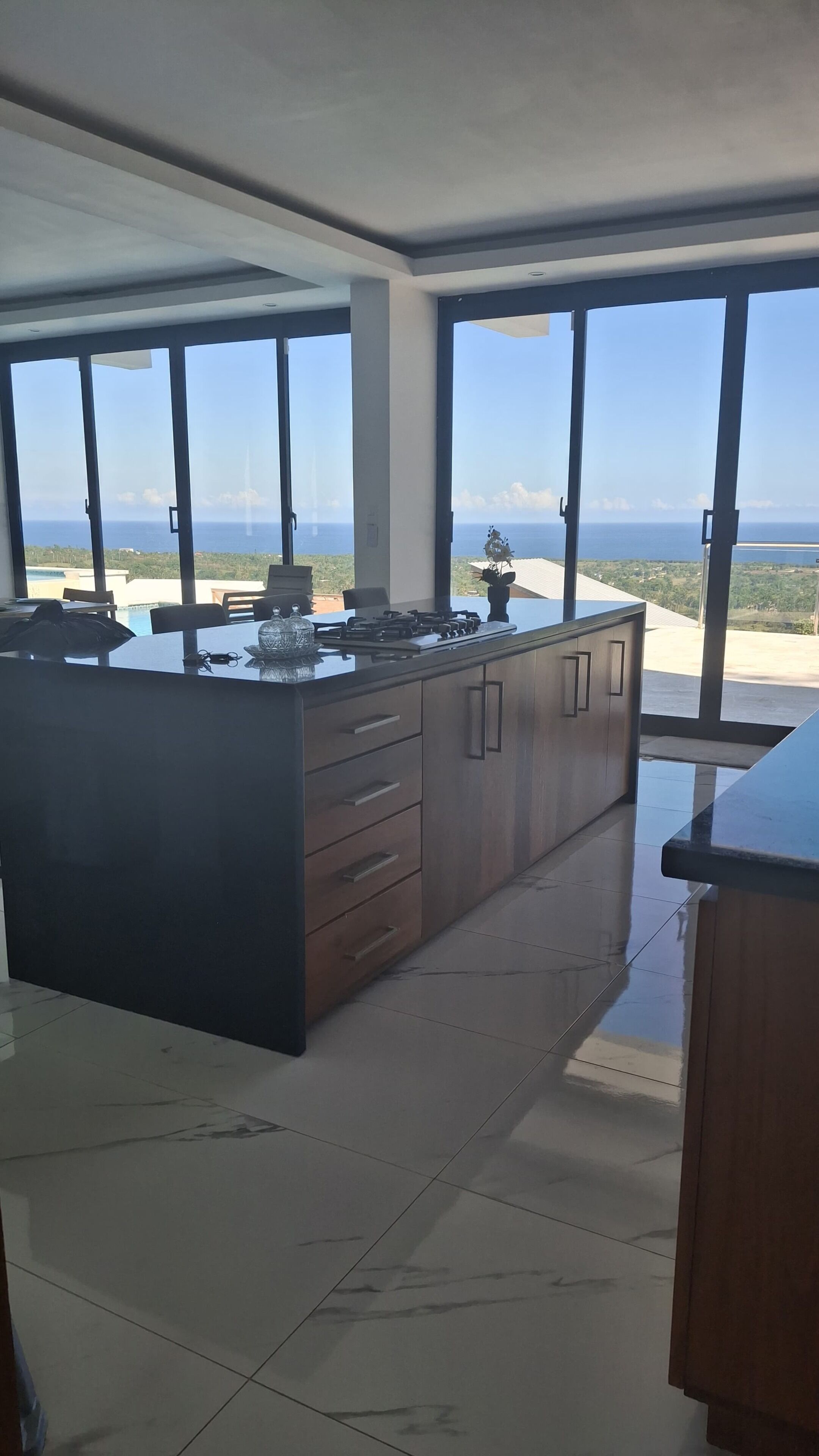 A modern kitchen with a large island, large windows, and a view of the ocean.