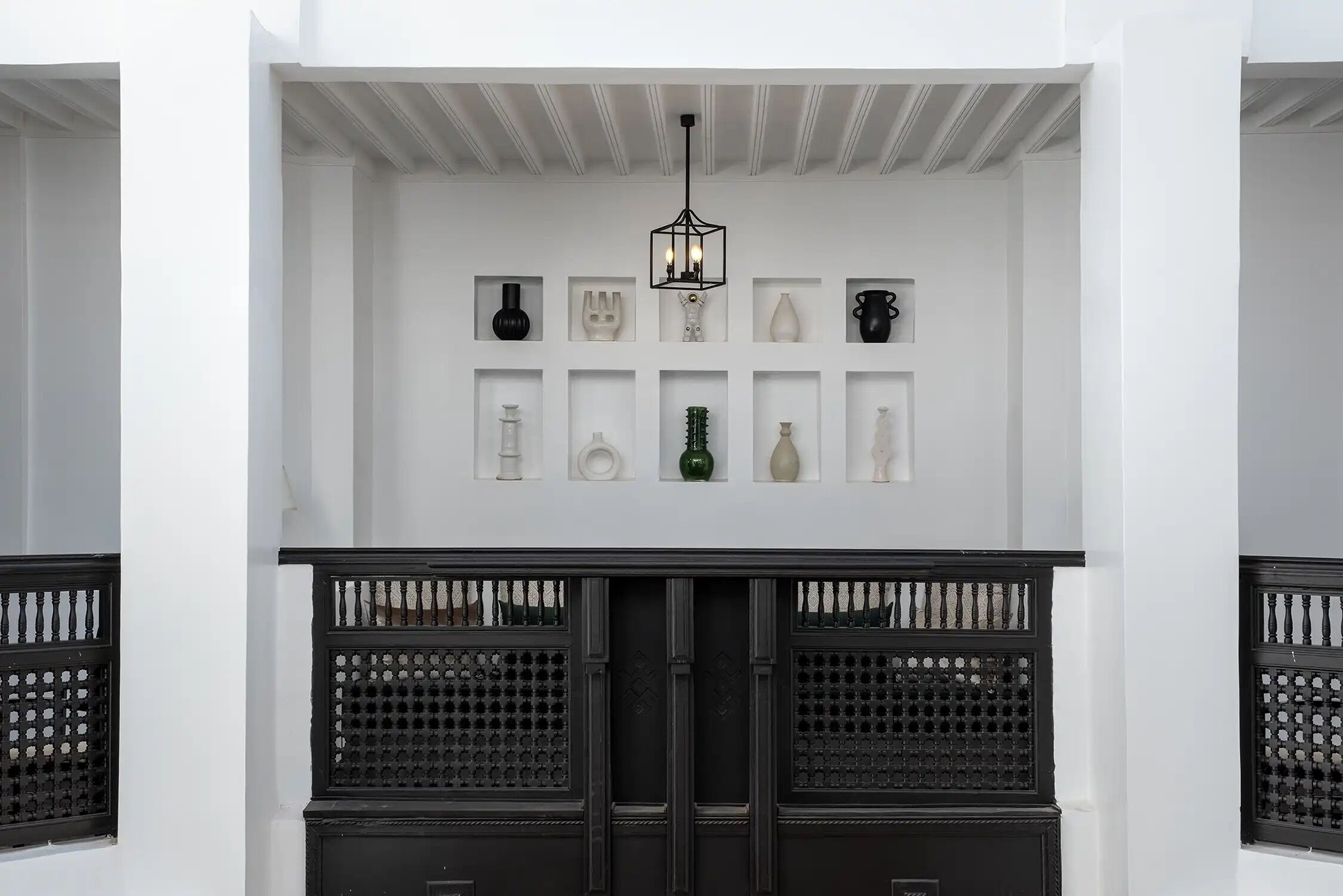 A white building with a black gate, a chandelier, and various vases on display.