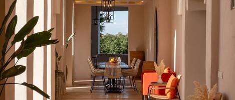 A dining area with a table and chairs, a window with a view, and a plant in the foreground.