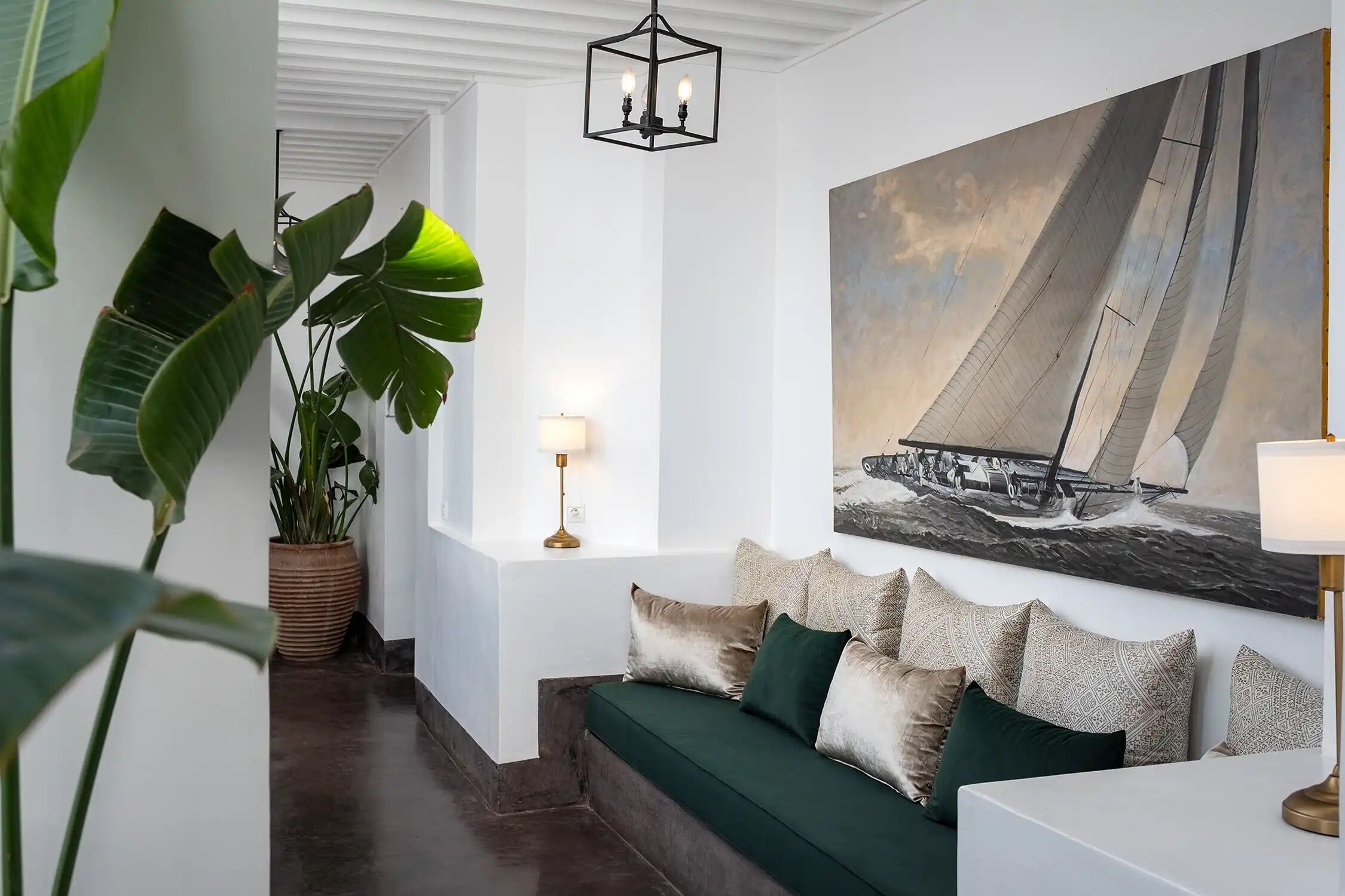 A modern living room with a green sofa, patterned cushions, a large sailboat painting, and a potted plant.