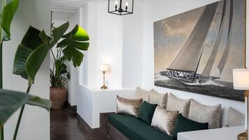 A modern living room with a green sofa, patterned cushions, a large sailboat painting, and a potted plant.