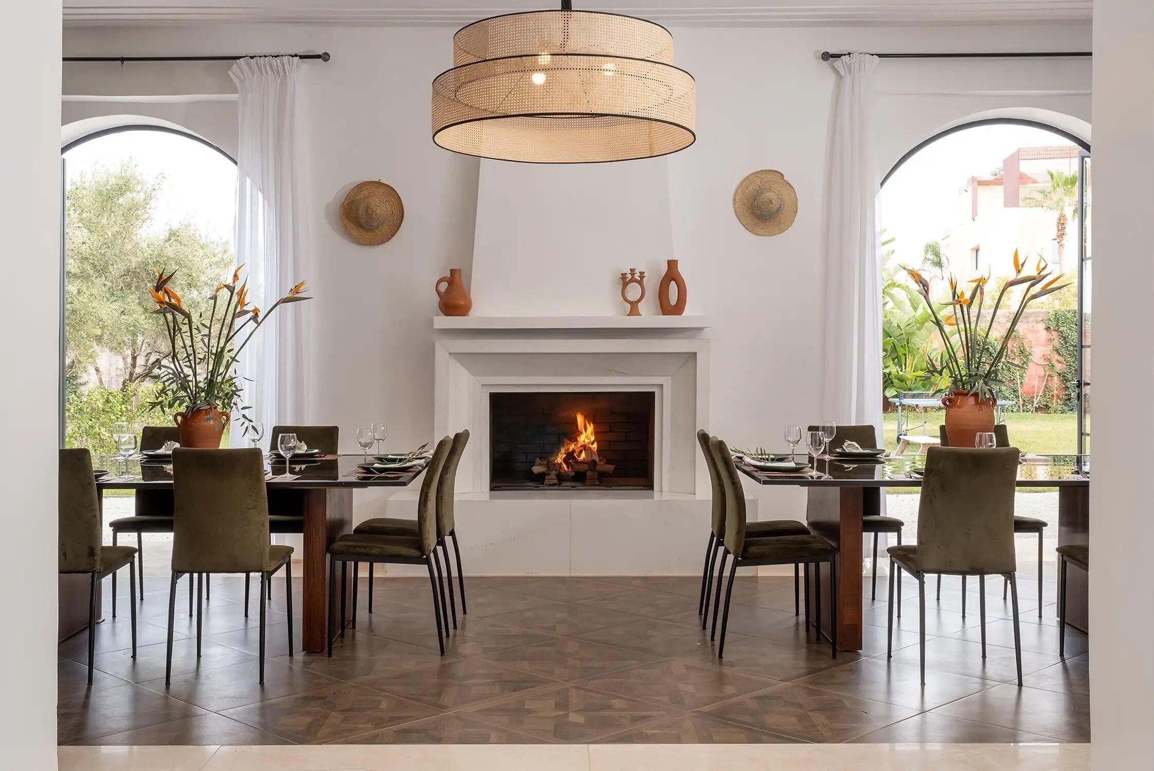 A dining area with a fireplace, two large windows, and a hanging light fixture.