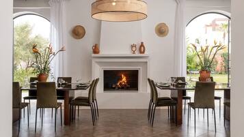 A dining area with a fireplace, two large windows, and a hanging light fixture.