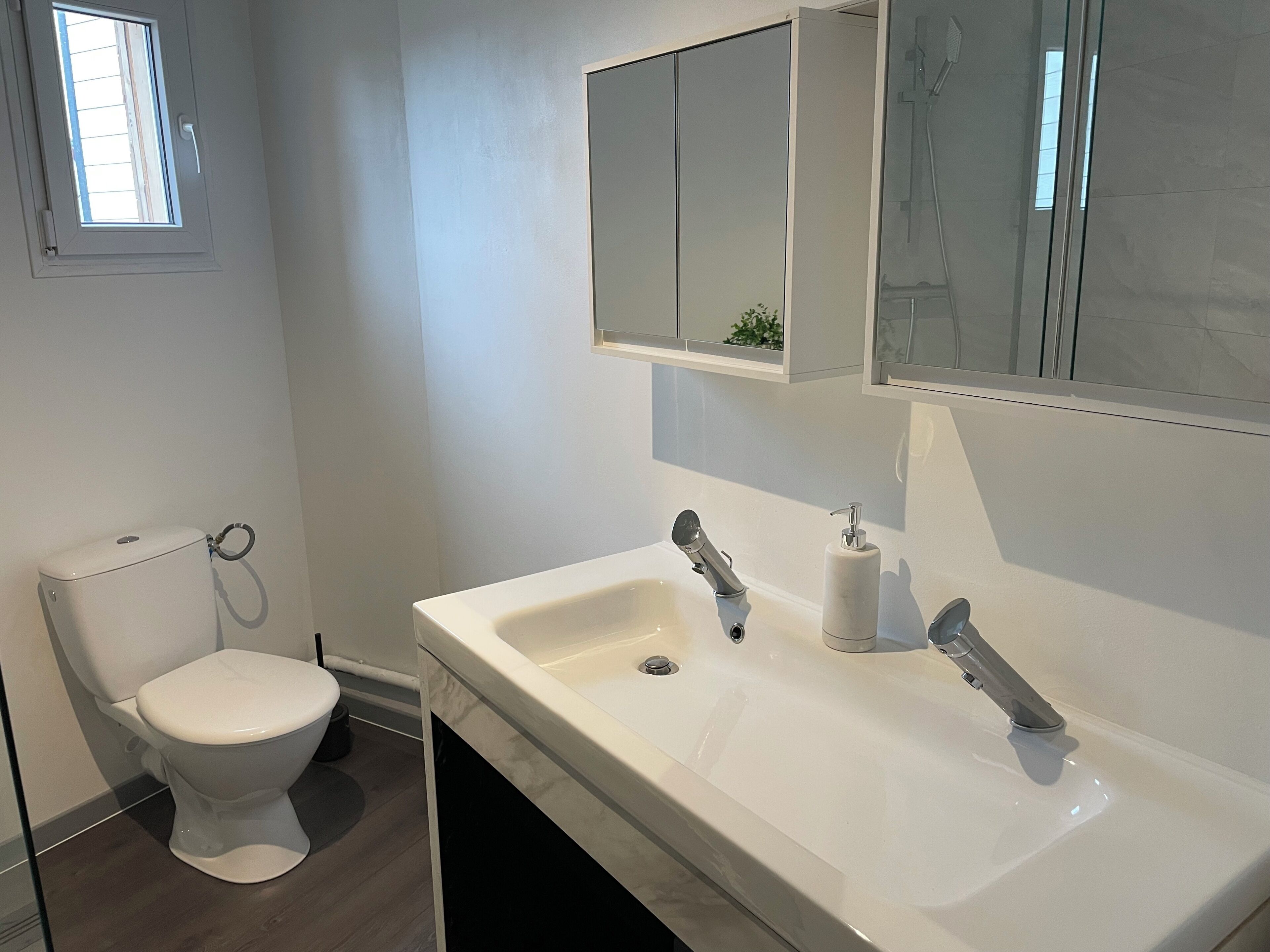 Une salle de bain avec des toilettes, un lavabo, un miroir et une fenêtre.