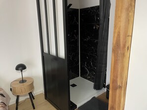 A room with a black and white striped partition, a small wooden stool with a lamp, and a black shower curtain. - New wooden house on the riverbank. (Vineuil)