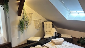 A bedroom with a bed, a chair, a macrame wall hanging, and a skylight.