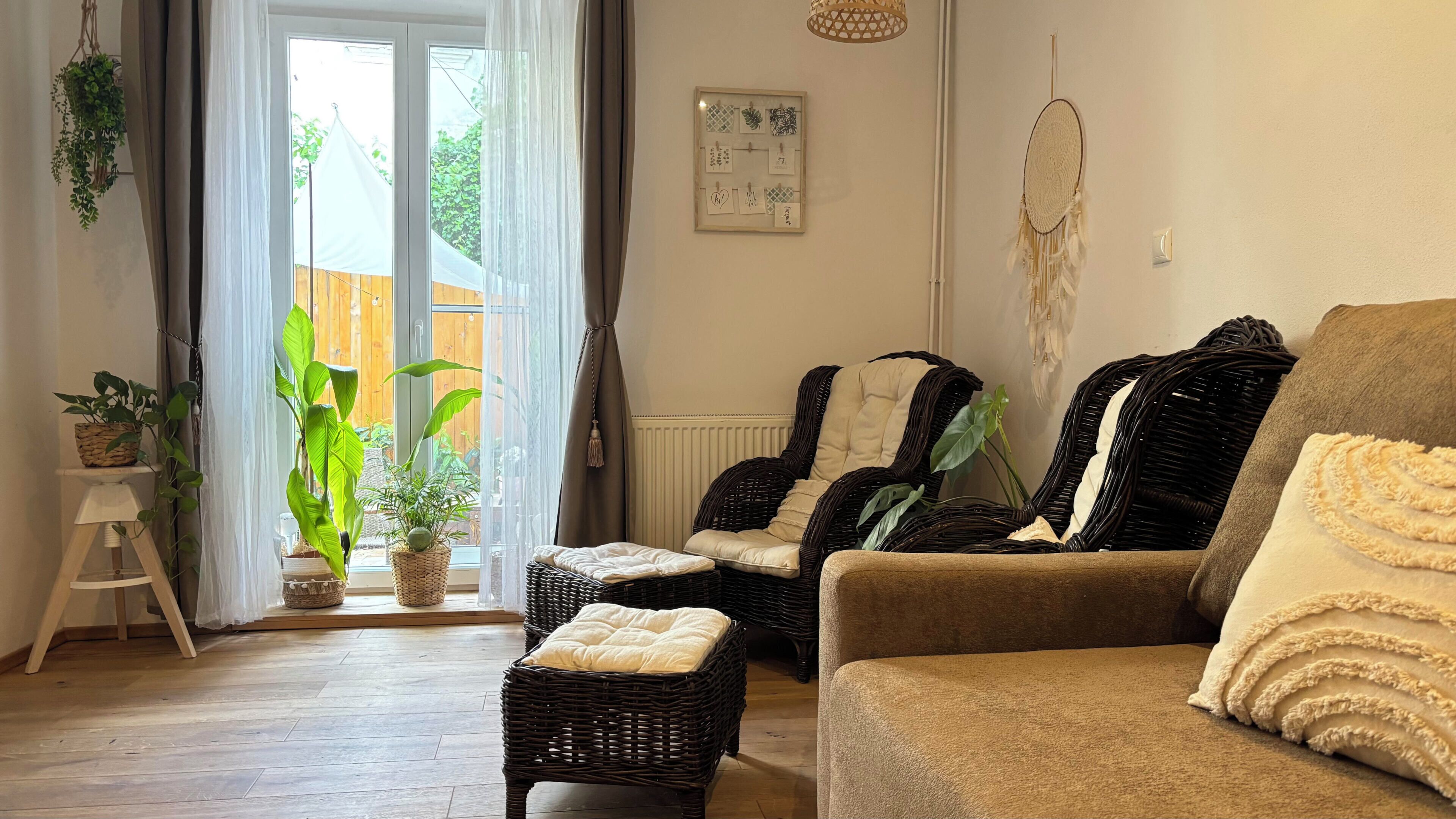 A living room with wicker furniture, a brown sofa, and a large window with curtains.