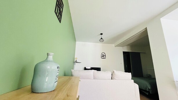 A room with a bed, a nightstand, a wall-mounted light fixture, and a door leading to another room. - "Sauge de Sarrail" City Center Apartment (Saintes)