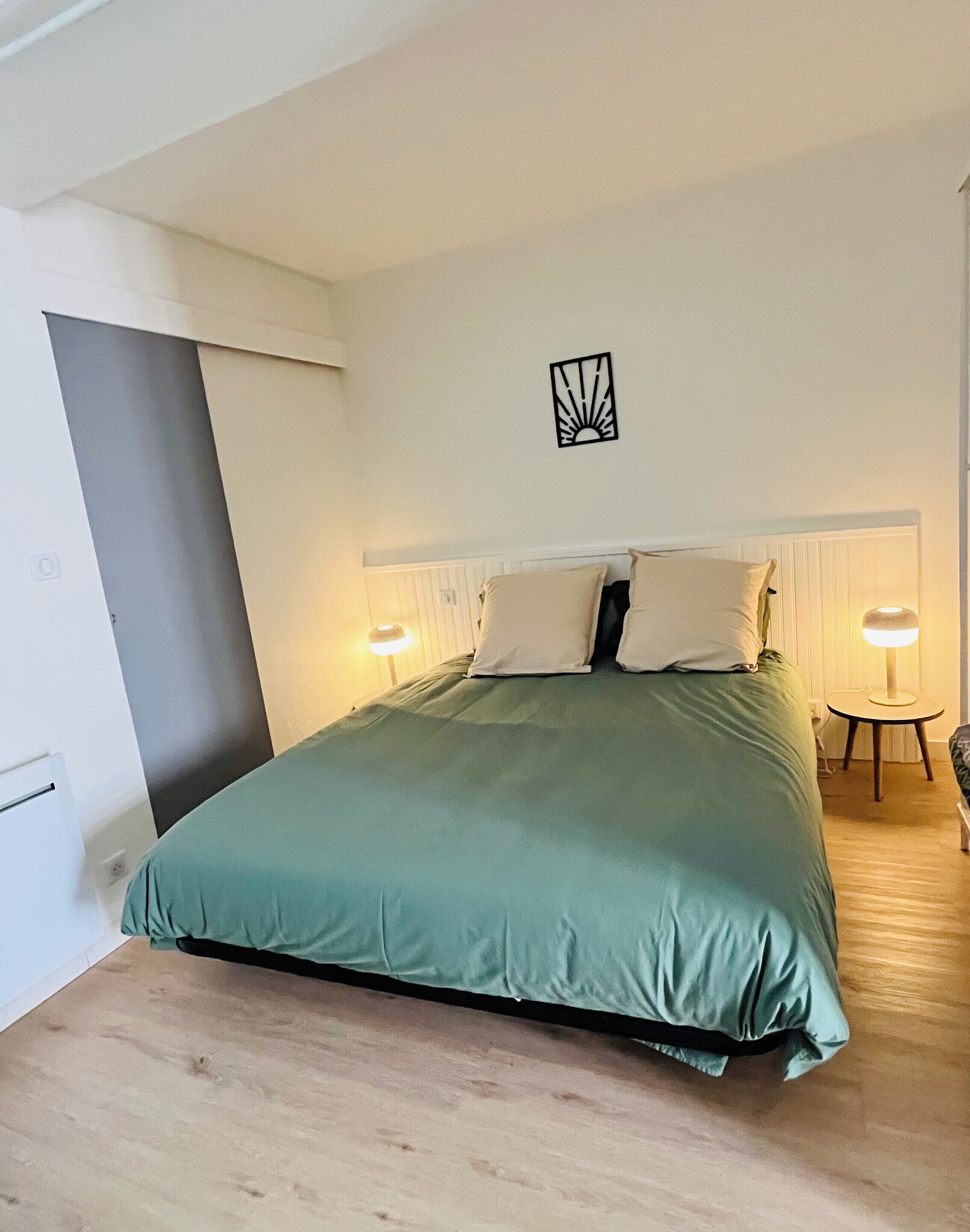 A bedroom with a bed, two bedside lamps, a wall-mounted light fixture, and a radiator.