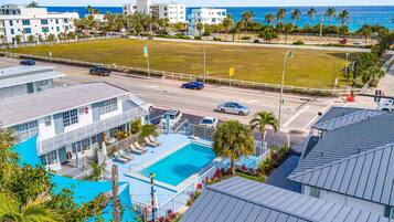 Um hotel com piscina, uma estrada com carros e vista para o oceano.