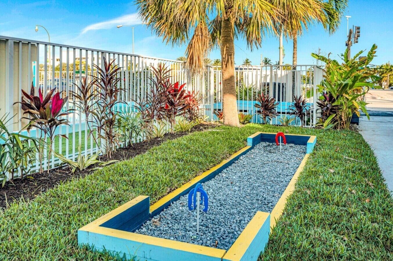 Un jardin avec un parterre rectangulaire, un palmier et une clôture blanche.