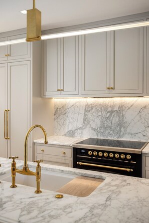 A kitchen with white cabinets, a marble countertop, a gold faucet, and a built-in stove. - Waterfront Luxury Home Downtown Traverse City (Traverse City)