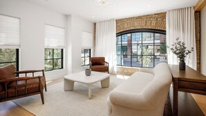 A modern living room with a sofa, armchair, and coffee table, large windows with blinds, a brick fireplace, and a view of the outside. - Waterfront Luxury Home Downtown Traverse City (Traverse City)